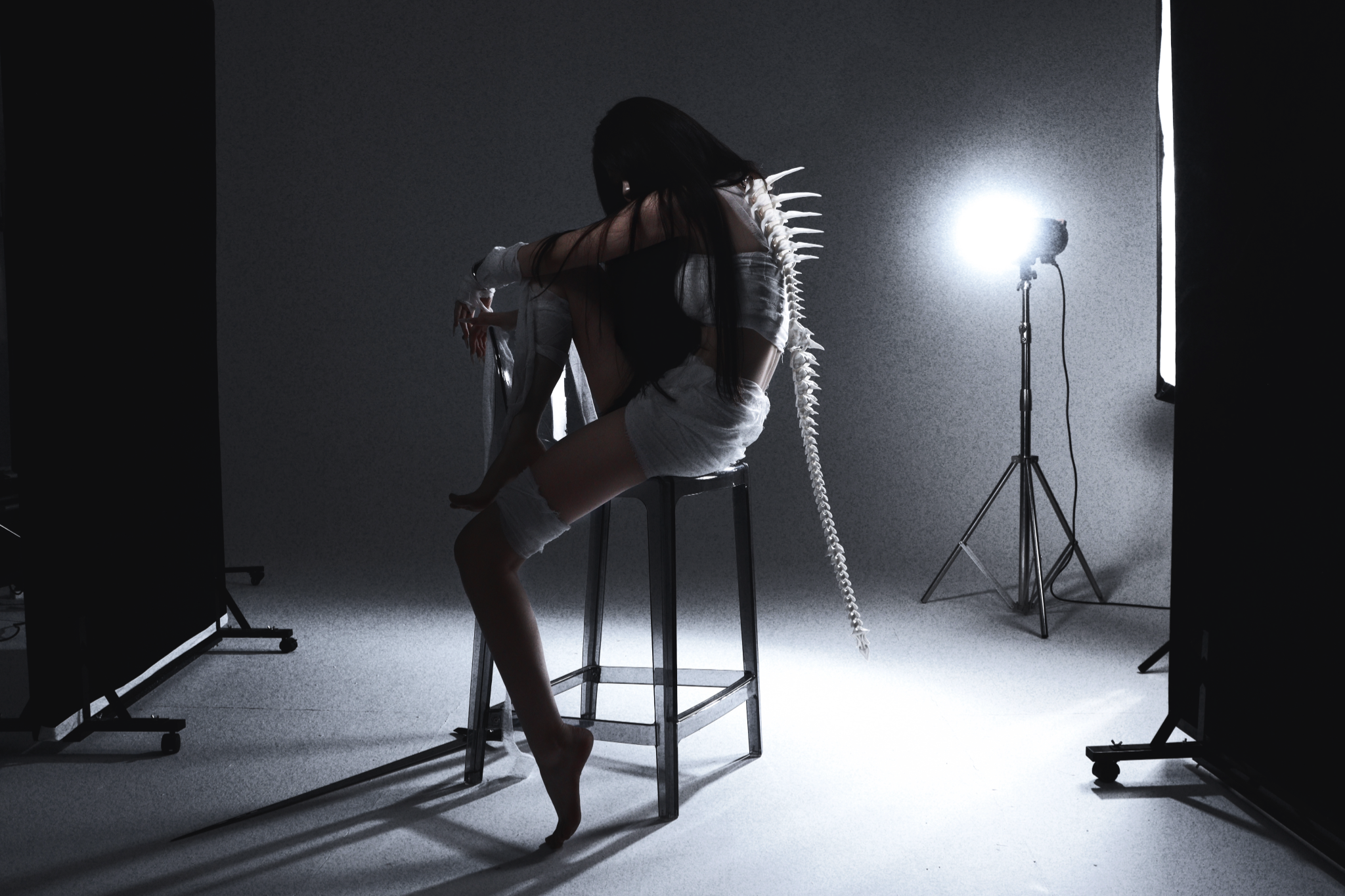 Wide studio photograph of a seated figure, with lighting equipment visible